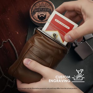 May include: A brown leather cigarette case with a metal clasp, holding a pack of filter cigarettes. A tin of beard balm and a lighter are also visible. The image includes the text "CUSTOM ENGRAVING".