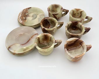 May include: A set of polished stone tea cups and saucers featuring swirling patterns of cream, light green, and dark brown. The collection includes multiple small handled cups and matching round saucers with smooth, glossy surfaces. Text reads housemarblecrafts.