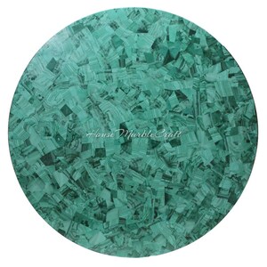 May include: A round tabletop with a mosaic pattern of green malachite. The surface is made of small, irregular pieces of the stone, creating a unique and textured appearance. The text "House Marble Craft" is visible.