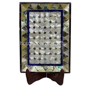 May include: Rectangular decorative piece with a mother-of-pearl mosaic design. The mosaic is framed by a dark border and a blue inner border. The piece is displayed on a wooden stand. The text "housemarblecrafts" is visible.