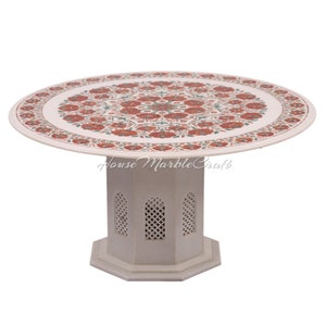 May include: A round, white marble table with a floral design in red and green. The table has a decorative, octagonal base with lattice-style cutouts. The table is approximately 30 inches in diameter.