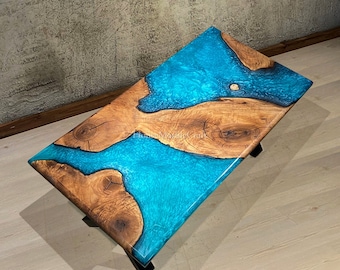 May include: Rectangular wooden coffee table with a vibrant turquoise epoxy resin river design. The wood has a natural grain pattern, and the table rests on black metal legs. A unique piece for any living space.
