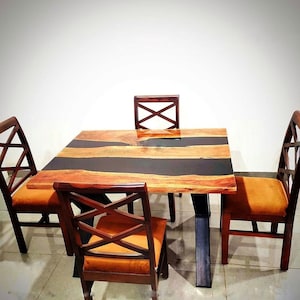 May include: A square dining table with a dark epoxy resin centre and four matching chairs. The table has a natural wood grain finish with a black resin inlay. The chairs have orange upholstered seats and wooden frames.