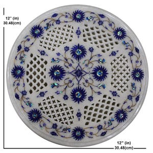 Puede incluir: Encimera de mesa redonda de mármol blanco, de 30,48 cm de diámetro, con intrincados diseños de incrustaciones florales y geométricas azules. El diseño incluye flores azules, hojas y varios patrones calados, creando una superficie decorativa.