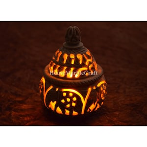 Peut inclure: Un bougeoir en pierre blanche avec des sculptures complexes d'éléphants et de motifs floraux. Le bougeoir est allumé et brille.