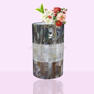 Puede incluir: Un jarrón cilíndrico decorativo con un diseño de mosaico, hecho de una mezcla de concha de abulón iridiscente y baldosas blancas de nácar. El jarrón contiene un ramo de flores blancas, rojas y rosas. El texto "House Marblecraft" es visible.