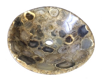 May include: Oval-shaped stone sink basin. The sink is made of various sizes of polished agate stones in shades of gray, brown, and cream. A circular drain hole is visible in the center. The sink has a natural, organic aesthetic.