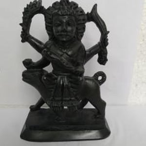 Puede incluir: Estatua negra de una deidad montando un jabalí. La deidad tiene cuatro brazos y lleva una corona y ropa elaborada. La estatua está hecha de un material liso y oscuro.