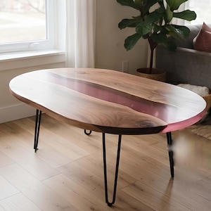 May include: An oval coffee table featuring a natural wood slab top with a translucent pink resin river running through the centre. The table is supported by four thin black metal hairpin legs that provide a stable base for the wooden surface.