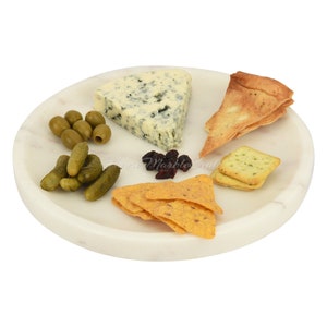 May include: A white marble serving platter with a selection of snacks. The platter features blue cheese, olives, pickles, crackers, tortilla chips, and dried cranberries. The round platter has a raised edge.