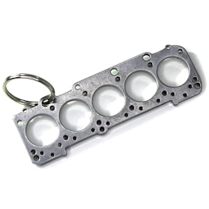 Peut inclure: Un porte-clés en métal argenté en forme de joint de culasse de moteur avec six trous de cylindre et un anneau de clé attaché.