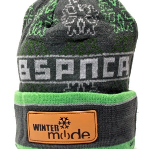 Könnte beinhalten: Graue und grüne Strickmütze mit einem weißen und grauen "ESPNCA"-Logo und einem braunen Lederpatch mit der Aufschrift "WINTER mode" und einem Schneeflockensymbol.