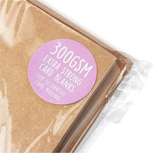 May include: A stack of brown card blanks, packaged in clear plastic. A round, light purple sticker on the package reads "300GSM EXTRA STRONG CARD BLANKS FOR DECORATIVE CARD MAKING."
