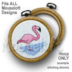 May include: A wooden embroidery hoop with a pink flamingo cross-stitch design. The hoop is 4 inches in diameter and is labelled "Fits ALL Mouseloft Designs".