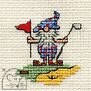 May include: A cross-stitch pattern featuring a gnome wearing a blue patterned hat and plaid pants, holding a golf club and standing next to a red flag. The gnome is positioned on a green patch of grass with a yellow sand trap nearby on a fabric background.