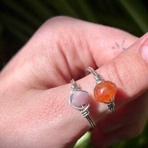 Peut inclure: Deux bagues en fil d'argent avec des pierres pr&eacute;cieuses roses et orange. Les bagues sont sur le doigt d'une personne.