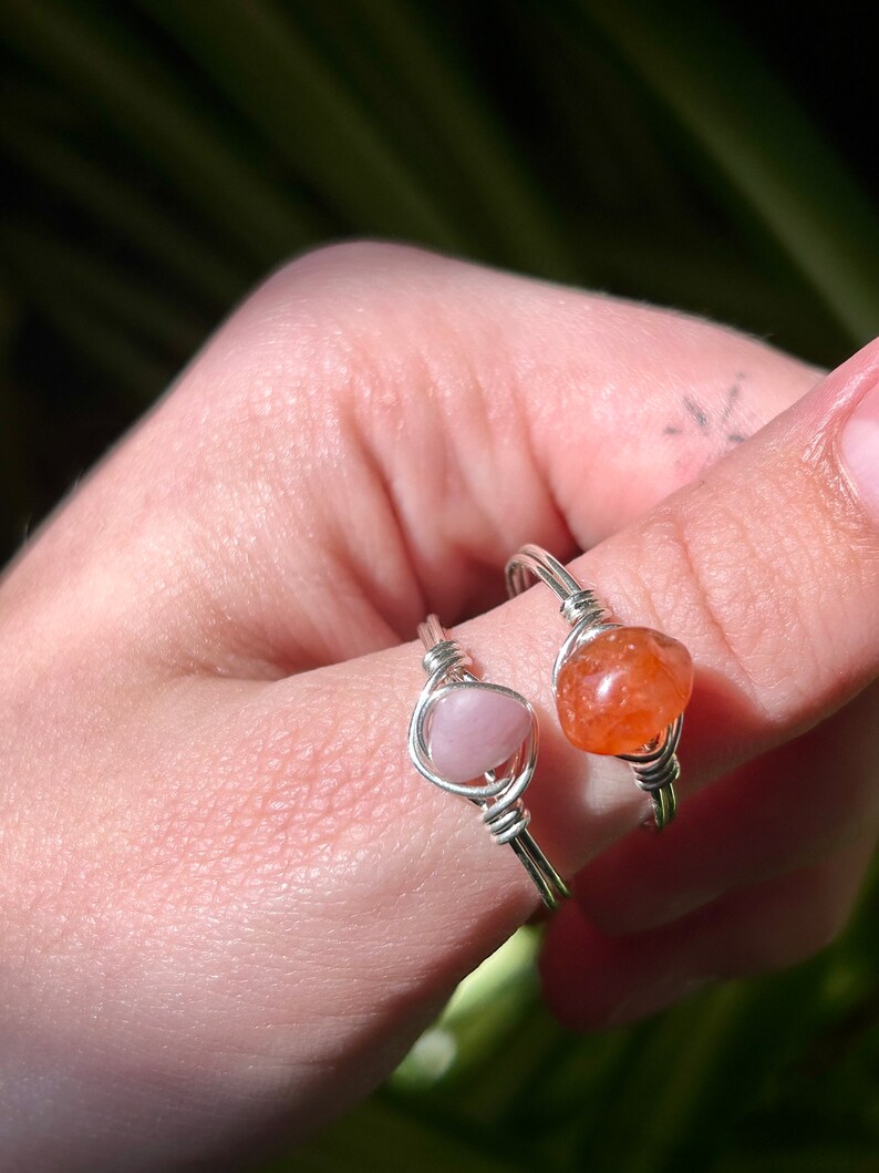 Peut inclure: Deux bagues en fil d'argent avec des pierres pr&eacute;cieuses roses et orange. Les bagues sont sur le doigt d'une personne.