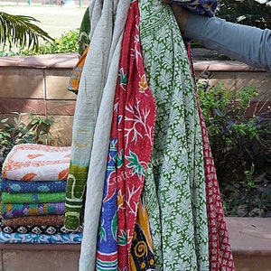 May include: A stack of colourful kantha quilts with floral and geometric patterns. The quilts are made from recycled saris and are ideal for adding a touch of bohemian style to your home.