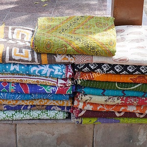Könnte beinhalten: Ein Stapel bunter Kantha-Steppdecken, ein traditionelles indisches handgenähtes Textil mit verschiedenen floralen und geometrischen Mustern. Die Decken werden aus recycelten Saris hergestellt und sind für ihre Langlebigkeit und Schönheit bekannt.