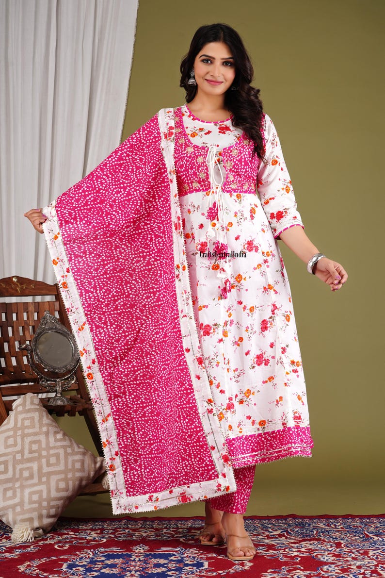 May include: A white and pink floral print kurta with a matching pink dupatta. The kurta has a round neckline and three-quarter sleeves. The dupatta has a white border with a pink and white polka dot pattern. The kurta and dupatta are made of cotton.
