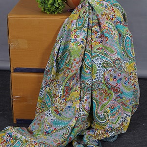 May include: A grey and white kantha quilt with a paisley pattern in shades of green, blue, red and yellow. The quilt is draped over a cardboard box and a terracotta pot.