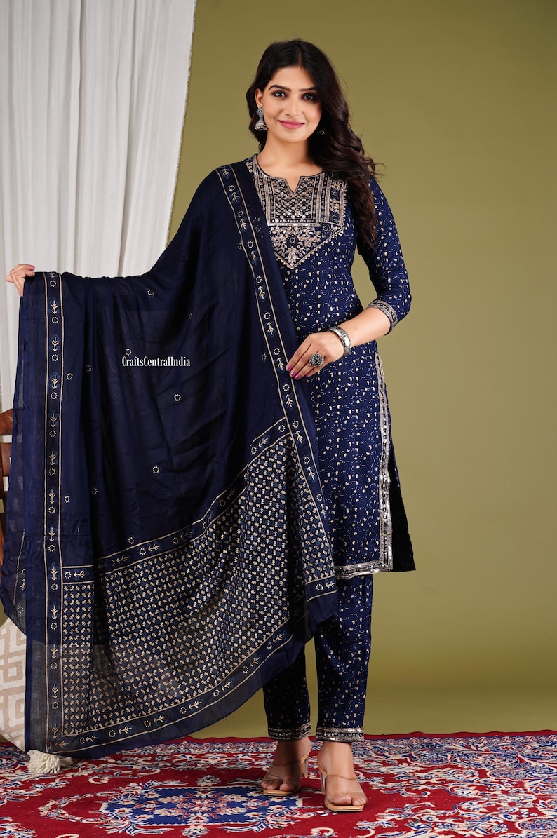 May include: A navy blue three-piece outfit with gold embroidery. The outfit includes a long-sleeved top, trousers, and a matching dupatta. The top has a round neckline and a decorative pattern on the front. The trousers are straight-legged and the dupatta is a sheer fabric with a border.