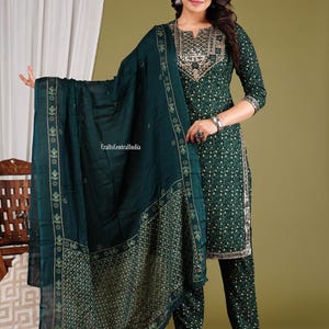 May include: A green salwar kameez set with gold embroidery and a matching dupatta. The set features a printed pattern throughout. The dupatta has a border with a floral design.