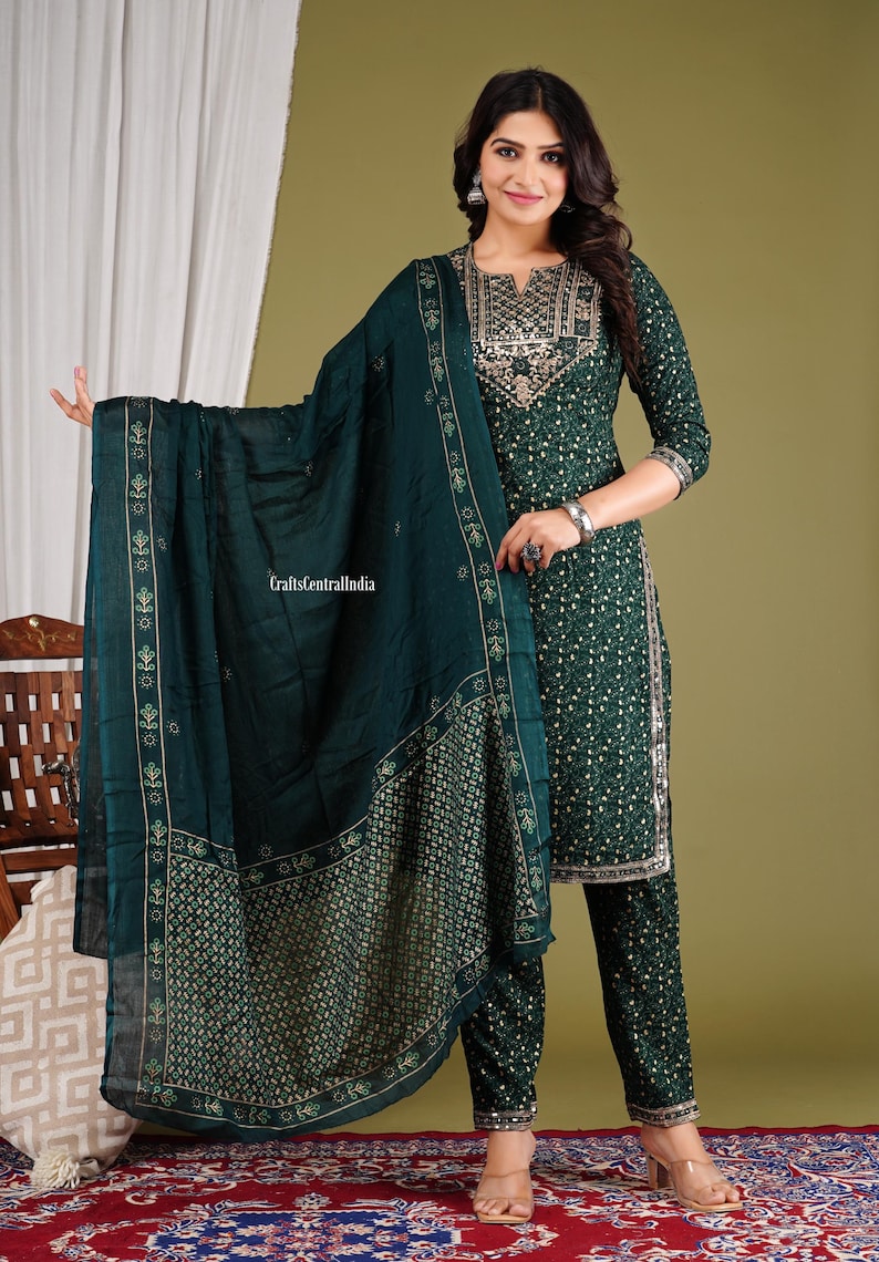 May include: A green salwar kameez set with gold embroidery and a matching dupatta. The set features a printed pattern throughout. The dupatta has a border with a floral design.