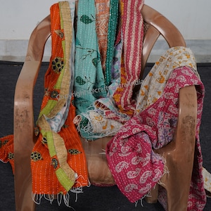 Puede incluir: Una colecci&oacute;n de colchas kantha de colores, hechas de saris reciclados, drapeada sobre una silla de madera. Las colchas presentan varios patrones y colores, incluyendo naranja, verde, azul, rosa y blanco.