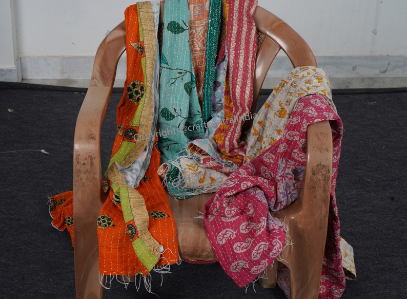 Puede incluir: Una colecci&oacute;n de colchas kantha de colores, hechas de saris reciclados, drapeada sobre una silla de madera. Las colchas presentan varios patrones y colores, incluyendo naranja, verde, azul, rosa y blanco.