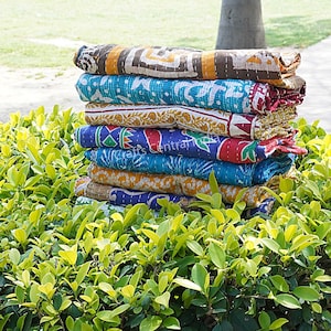 May include: A stack of six colorful kantha quilts, made from recycled saris, with intricate patterns and stitching. The quilts are folded and stacked on top of each other, creating a visually appealing display.