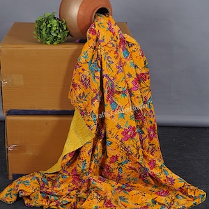 May include: A yellow kantha quilt with a floral and bird print. The quilt is draped over a box and a terracotta pot.