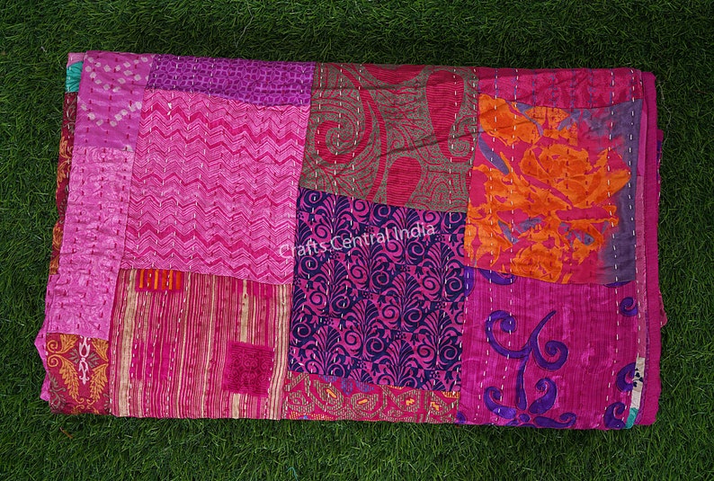 May include: A patchwork quilt made from colorful silk fabric scraps. The quilt is pink, purple, orange, and brown. The quilt is hand-stitched and has a unique, handmade look. "Crafts Central India" is printed on the quilt.
