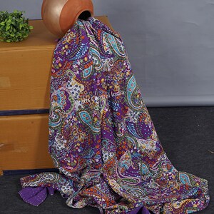 May include: A purple kantha quilt with a paisley pattern and colourful floral accents. The quilt is draped over a brown box and a terracotta pot.