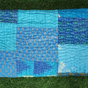 Könnte beinhalten: Eine gefaltete Patchwork-Steppdecke in Blautönen. Die Steppdecke weist verschiedene Muster und Texturen auf, darunter florale Designs und unifarbene Abschnitte. Der Text "Crafts Central India" ist sichtbar.