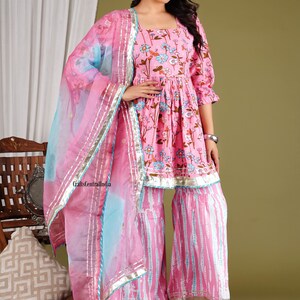 Op de afbeelding: Een roze en blauwe salwar kameez met een bloemenprint en een bijpassende dupatta. De kameez heeft een vierkante halslijn en 3/4 mouwen. De salwar is een wijde broek met een uitlopende zoom. De dupatta is een dunne sjaal met een bloemenprint.