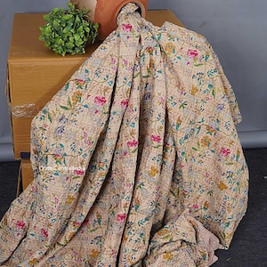 May include: A beige cotton quilt featuring a dense, multicolored floral pattern with pink, yellow, blue, and green blossoms and leaves. The fabric displays visible running stitch embroidery throughout, creating a textured, quilted appearance.