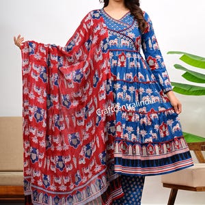Könnte beinhalten: Ein blau-rotes indisches Anzug-Set mit passendem Schal. Der Anzug hat ein detailliertes Muster aus Elefanten und floralen Designs. Der Text "craftcentralindia" ist auf dem Schal zu sehen. Das Outfit beinhaltet ein langärmliges Oberteil und eine passende Hose.