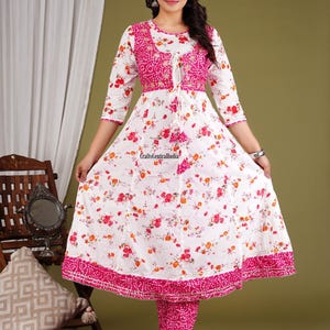 May include: A white and pink floral print dress with a pink embroidered bodice and a matching pink palazzo pant. The dress has a round neckline and three-quarter sleeves. The palazzo pant has a straight leg and a pink floral print.