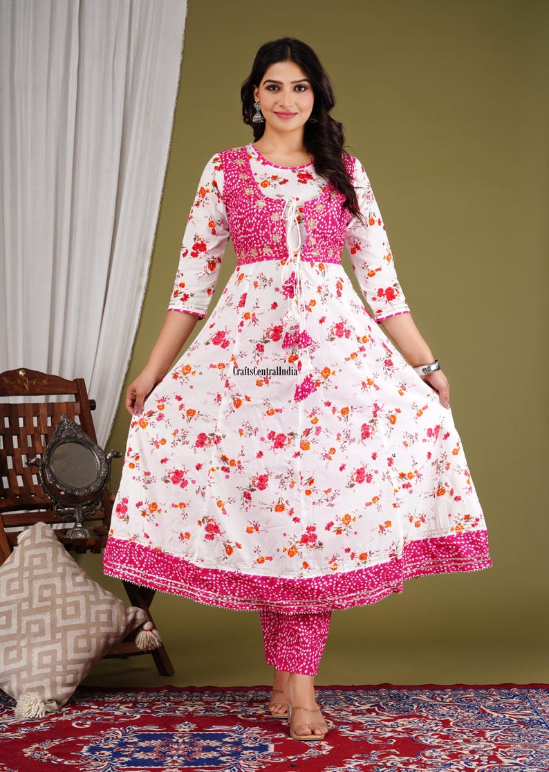 May include: A white and pink floral print dress with a pink embroidered bodice and a matching pink palazzo pant. The dress has a round neckline and three-quarter sleeves. The palazzo pant has a straight leg and a pink floral print.