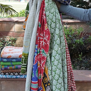 May include: A stack of colorful kantha quilts with floral and geometric patterns. The quilts are made of recycled saris and are perfect for adding a touch of bohemian style to your home.