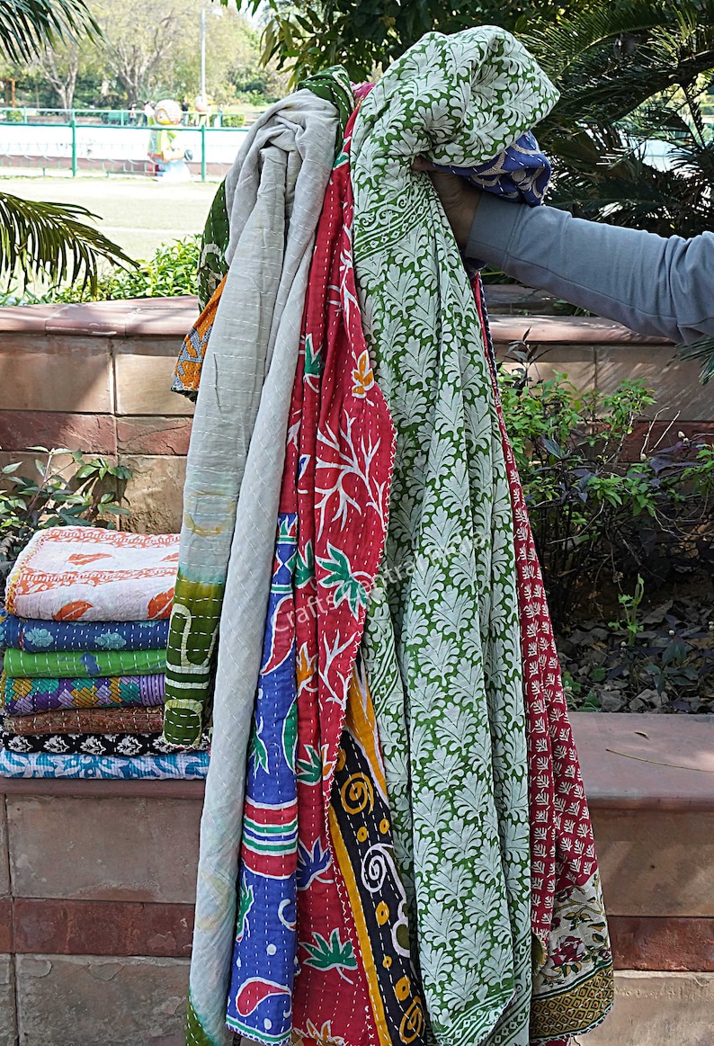 May include: A stack of colorful kantha quilts with floral and geometric patterns. The quilts are made of recycled saris and are perfect for adding a touch of bohemian style to your home.