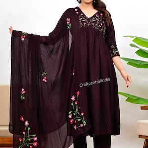 Könnte beinhalten: Ein dunkelburgunderfarbenes Salwar-Kameez-Set mit floraler Stickerei. Das Set beinhaltet eine langärmlige Tunika, eine passende Hose und einen transparenten Dupatta. Die Tunika und der Dupatta weisen rosa und grüne Blumenstickereien auf. Der Text "Craftcentralindia" ist sichtbar.