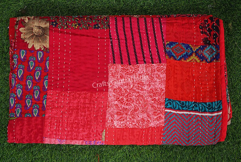 May include: A red and blue patchwork quilt with a variety of patterns, including paisley, floral, and geometric designs. The quilt is made of recycled saris and is hand-stitched.