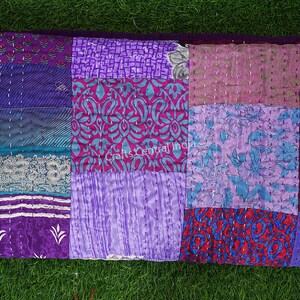 May include: A patchwork quilt made from repurposed saris in shades of purple, pink, blue, and red. The quilt is hand-stitched and has a variety of floral and geometric patterns.