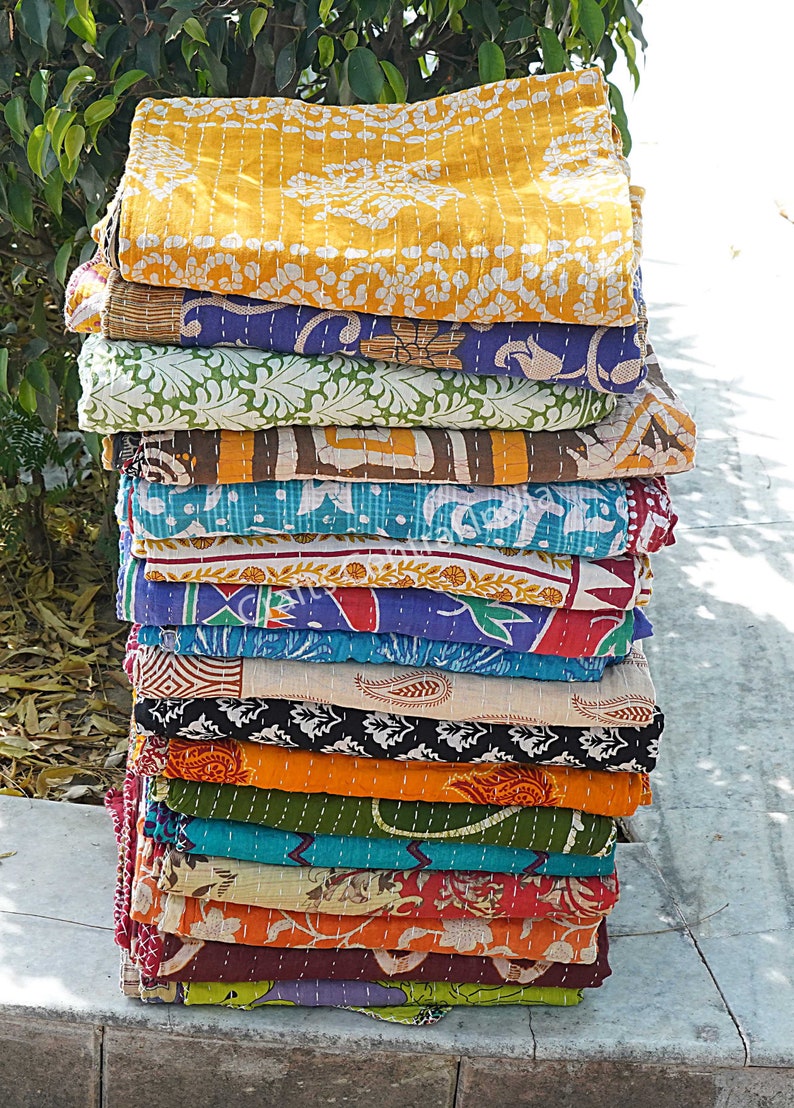May include: A stack of colorful kantha quilts with various floral and geometric patterns. The quilts are made of recycled saris and are hand-stitched.