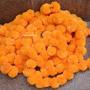 May include: A garland of bright orange marigold flower blossoms, arranged in a circular shape. The garland is made of artificial flowers and is perfect for decorating for a special occasion.
