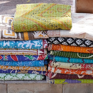 May include: A stack of colorful kantha quilts with various patterns, including paisley, floral, and geometric designs. The quilts are made of cotton and are hand-stitched.