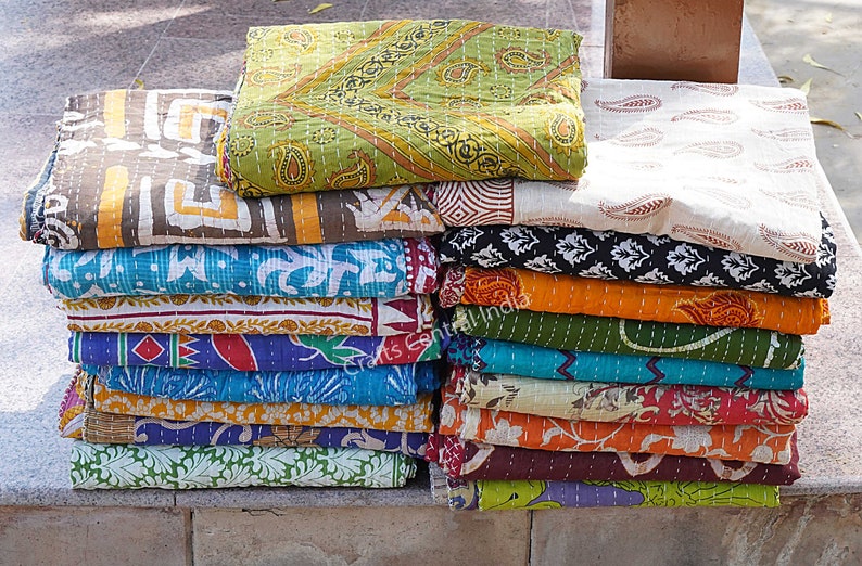 May include: A stack of colorful kantha quilts with various patterns, including paisley, floral, and geometric designs. The quilts are made of cotton and are hand-stitched.