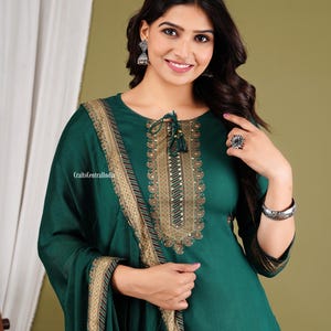 May include: A woman wearing a teal green kurta with gold embroidery and a matching dupatta. The kurta has a round neckline and a tie-up detail at the neck. The dupatta has a gold border and a red and gold stripe.